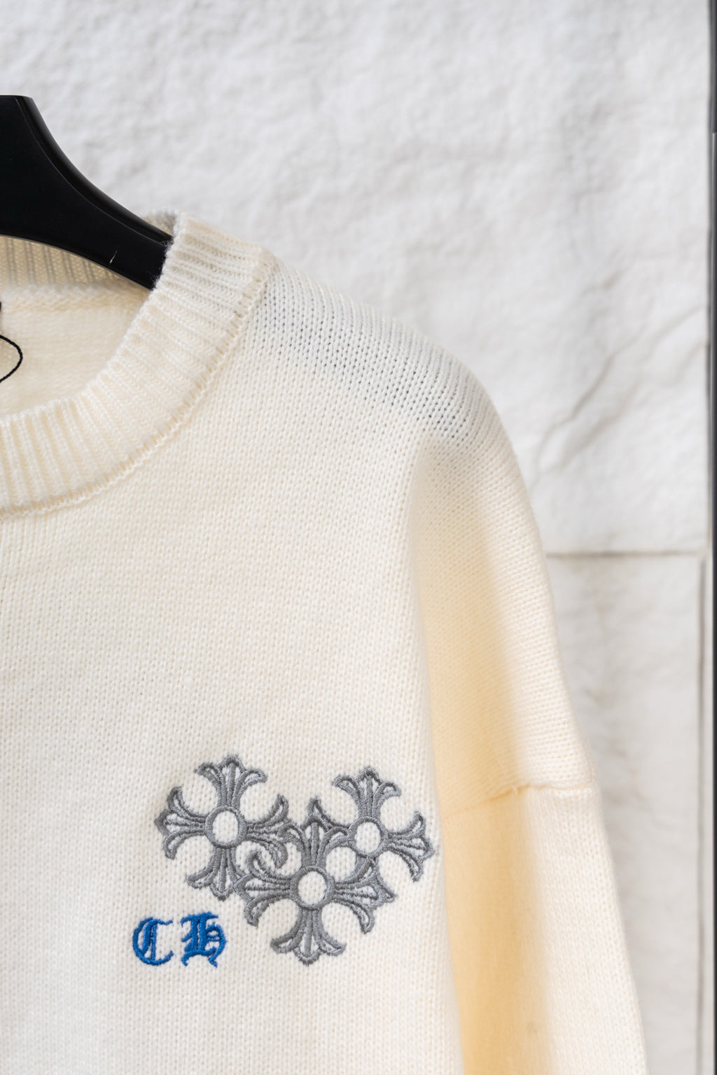 Cream knit long sweater with ribbed neckline and gray-blue embroidered crest