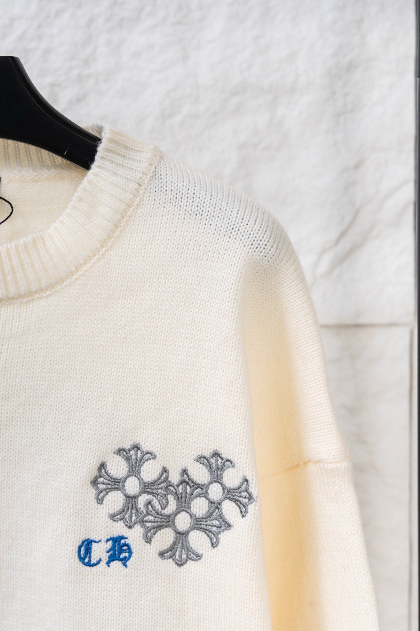 Cream knit long sweater with ribbed neckline and gray-blue embroidered crest