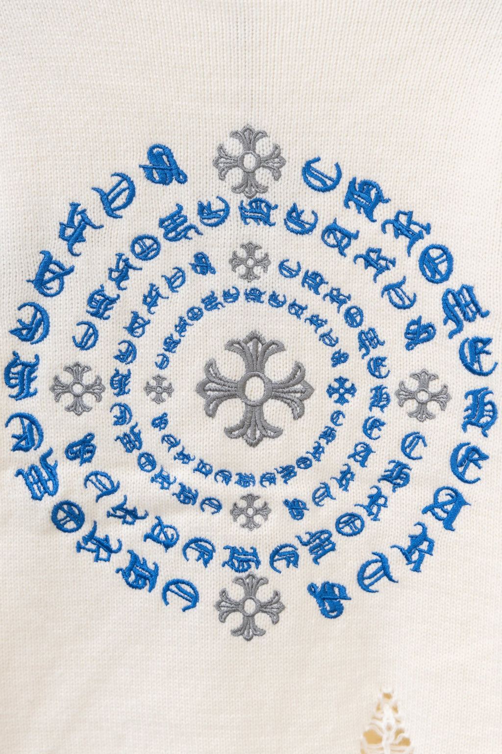 Close-up of blue and gray circular embroidery on a cream knit sweater