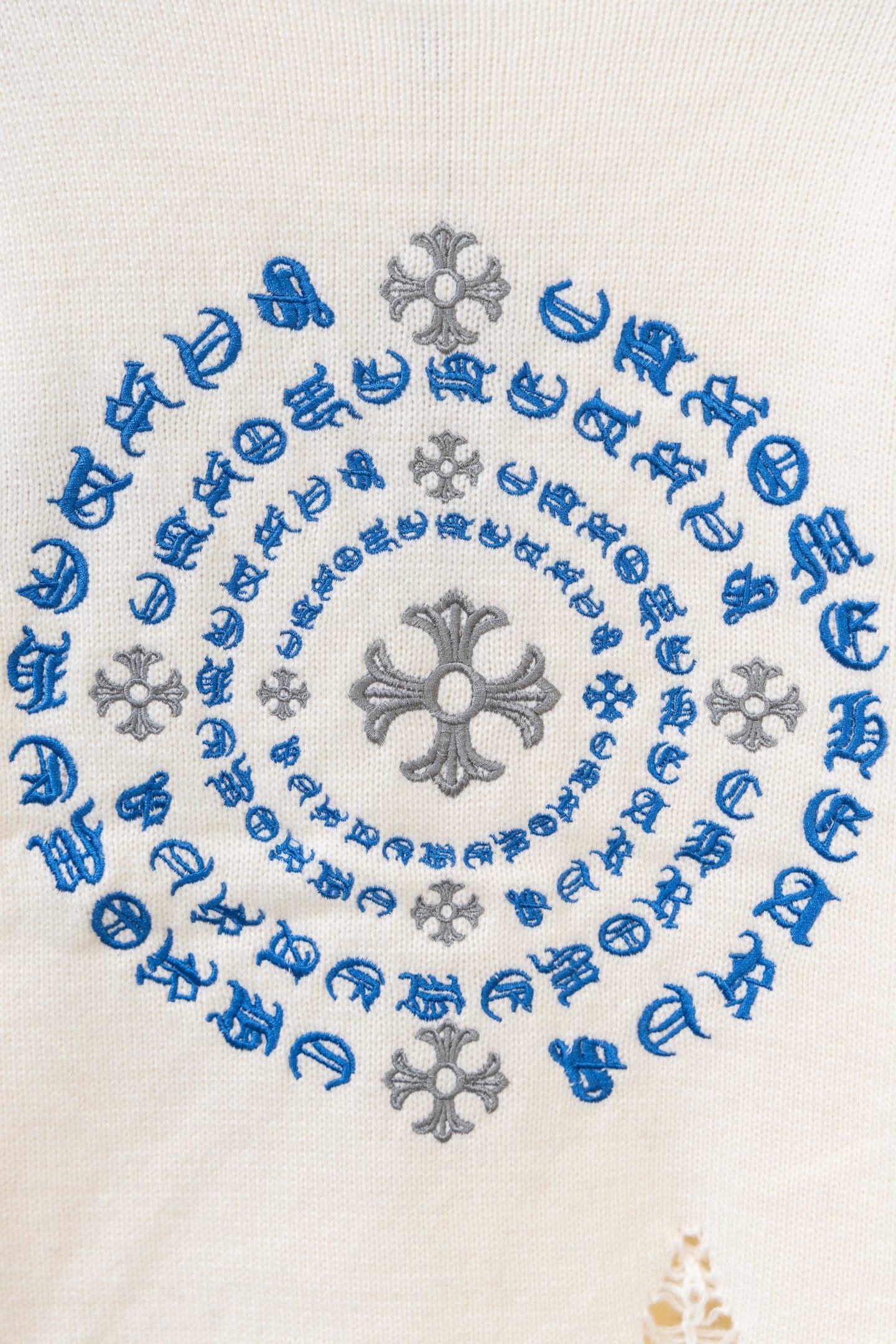 Close-up of blue and gray circular embroidery on a cream knit sweater
