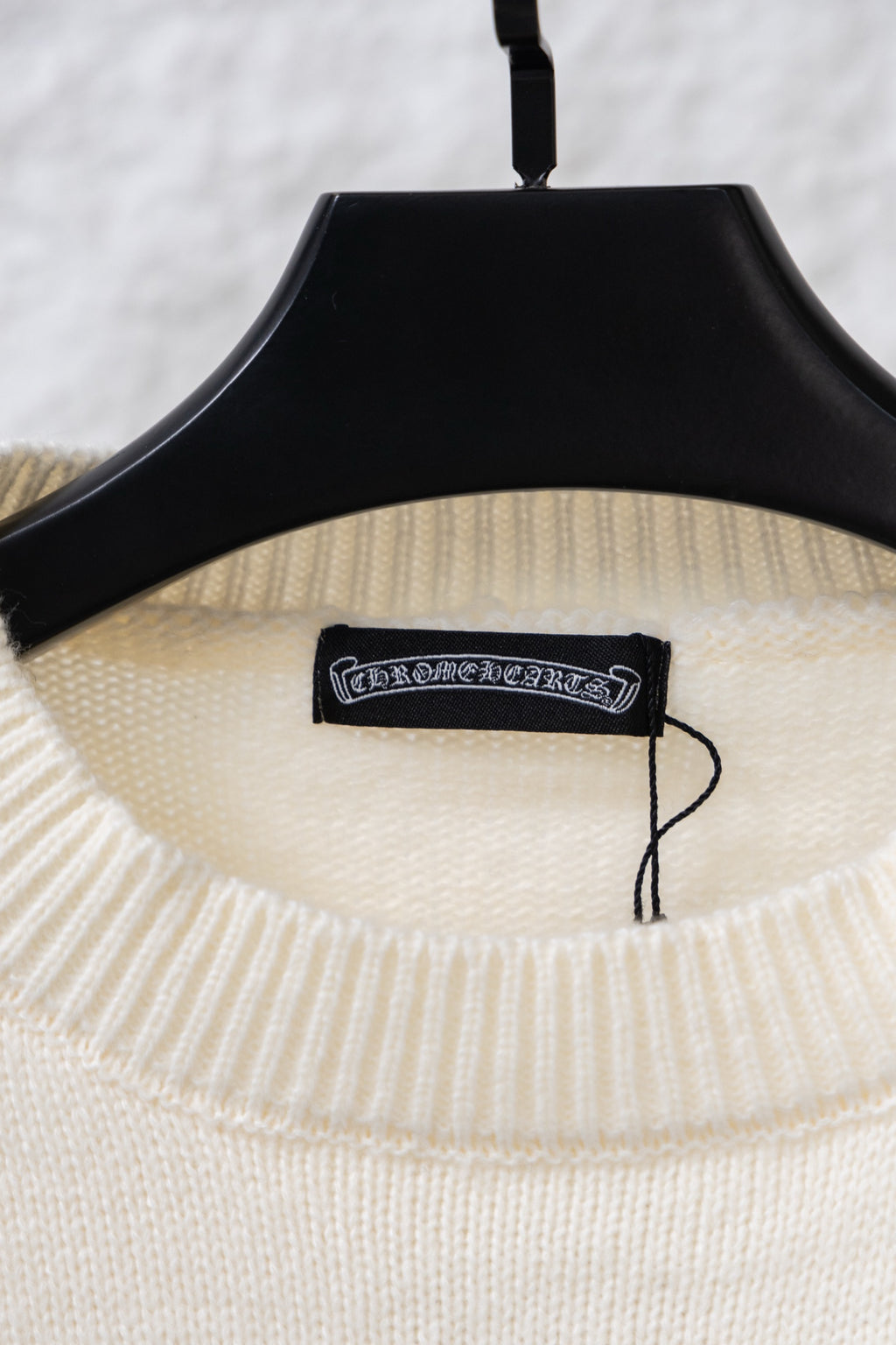 Cream knit sweater neckline with black brand tag on a hanger