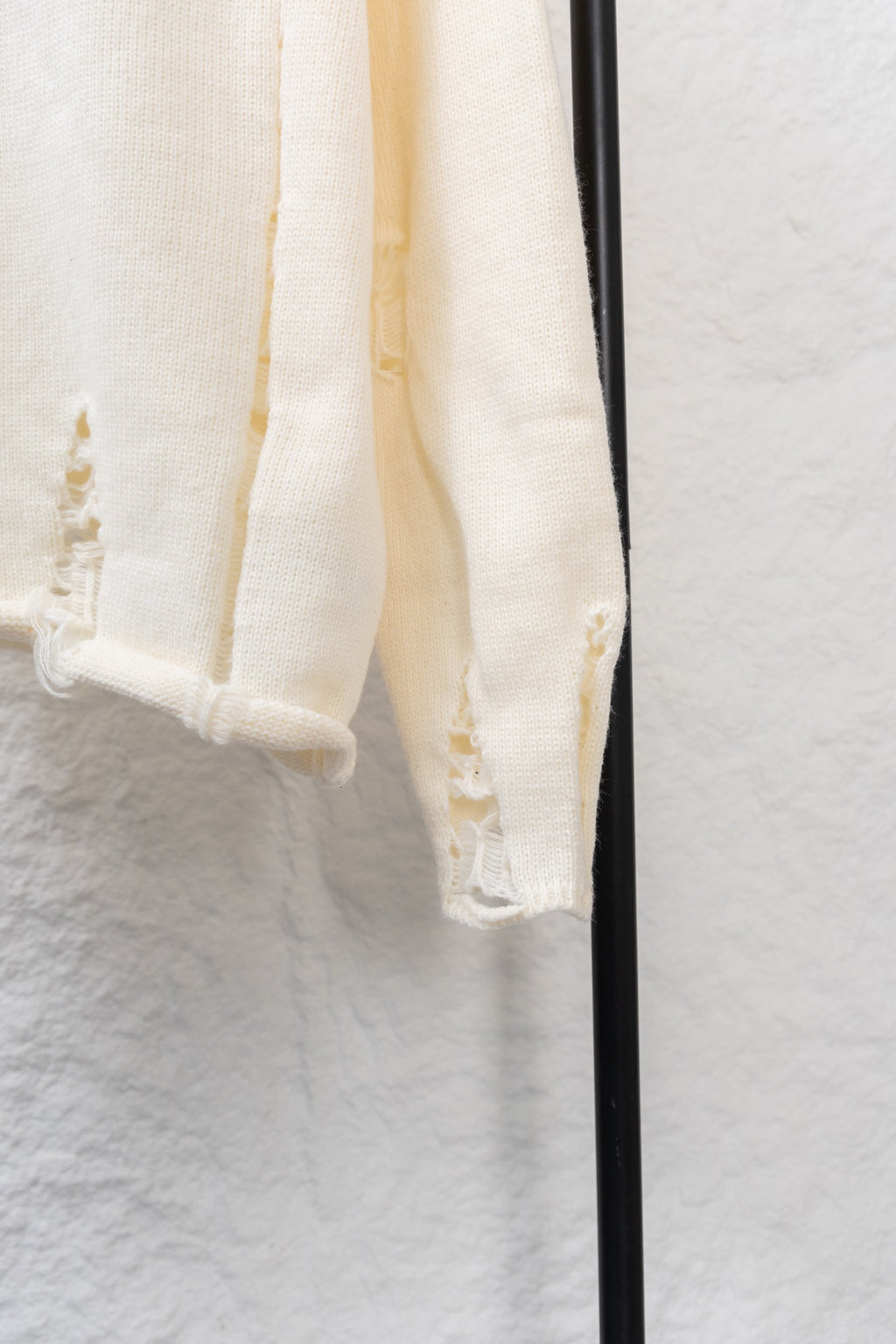 Cream knit sweater sleeve hem with small cutout and embroidery details