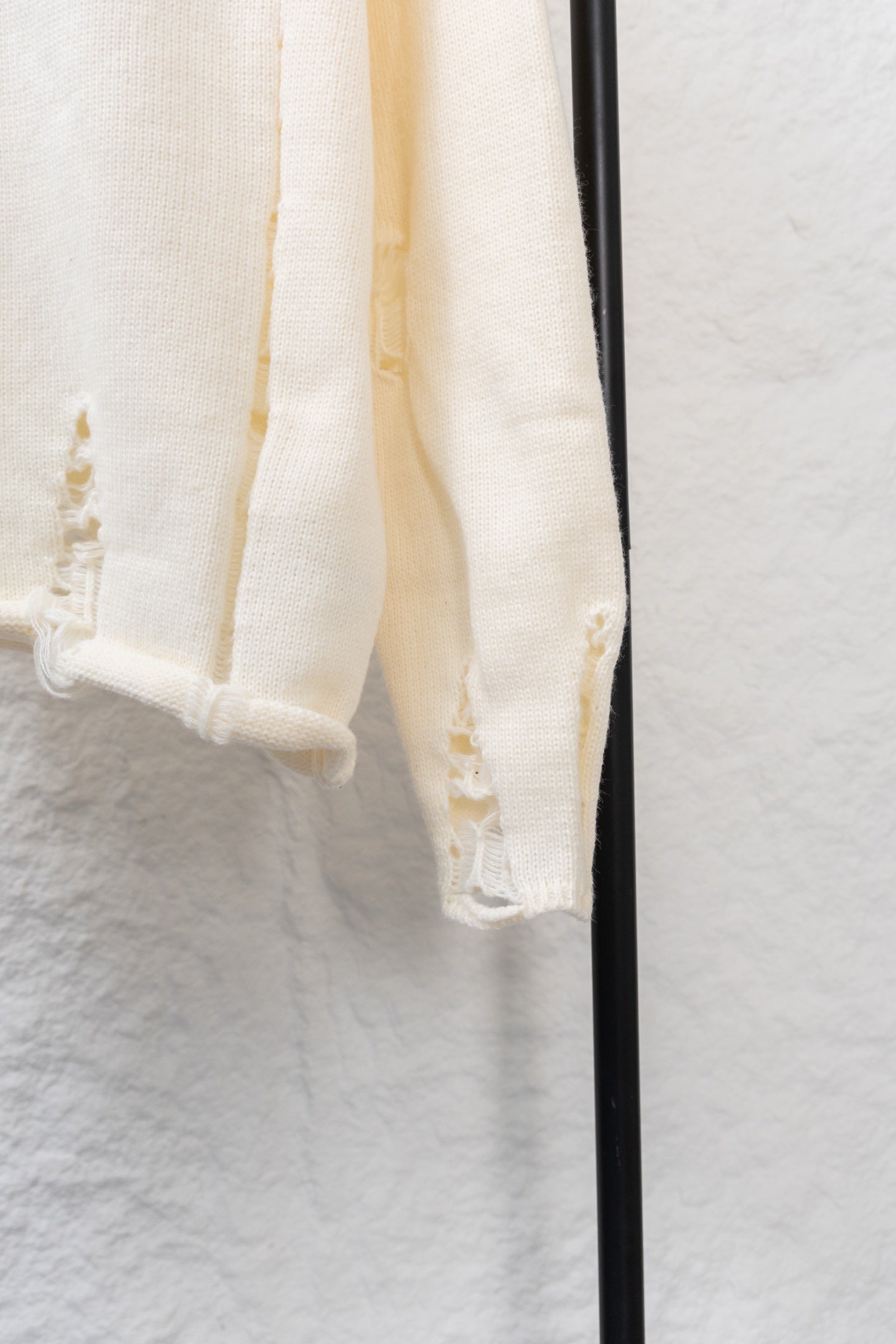 Cream knit sweater sleeve hem with small cutout and embroidery details