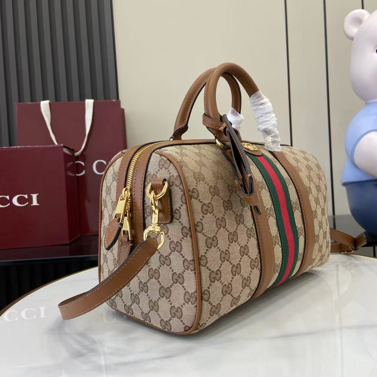 Gucci duffel bag side view with GG canvas print, green and red web stripe, leather straps