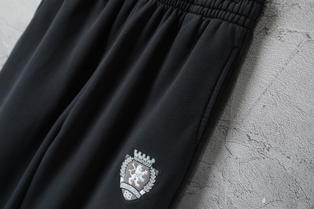Black elastic-waist pants with embroidered crest logo on front leg