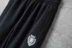 Dark pants with elastic waistband and crest logo patch near the left thigh