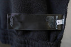 Zip-up jacket inner label and size tag on dark fabric.