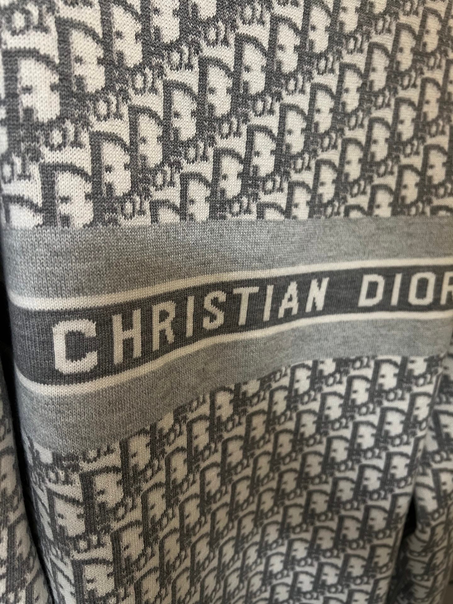 Close-up of “CHRISTIAN DIOR” lettering on light gray monogram knit sweater