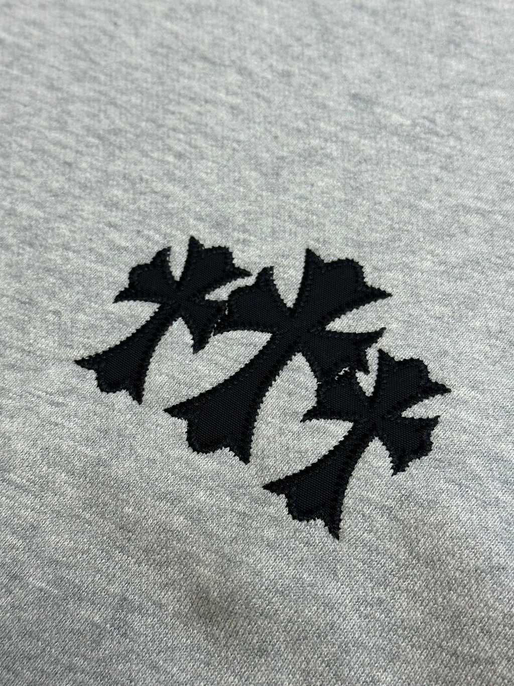 Light gray sweatshirt fabric with three-leaf black logo patch