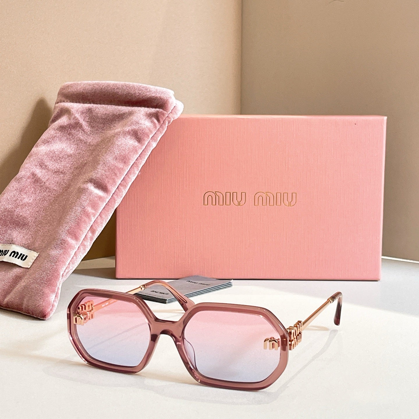 MiuMiu sunglasses with rose-tinted oversized frames, light lenses, and gold logo detailing