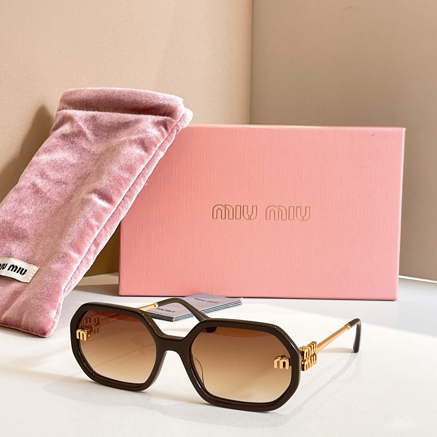 MiuMiu sunglasses with black oversized frames, brown-tinted lenses, and gold logo detailing