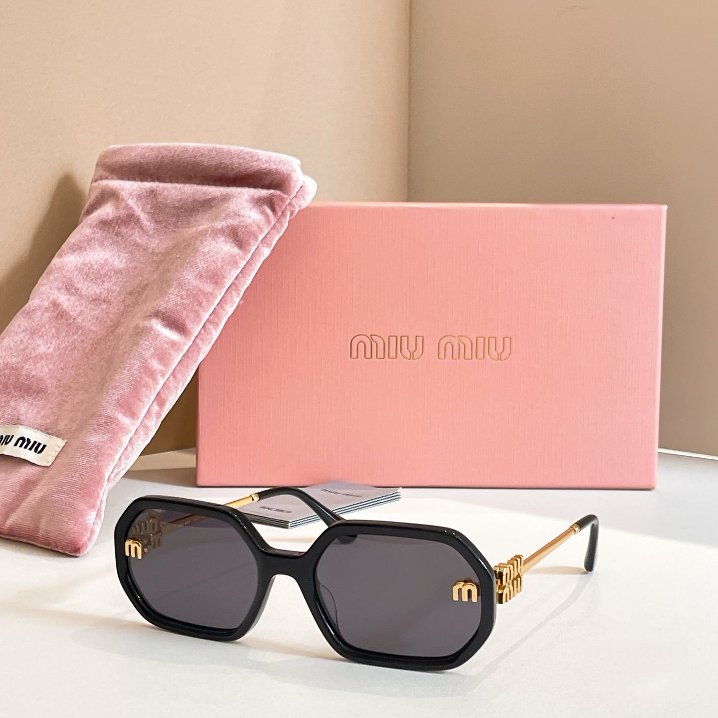 MiuMiu sunglasses with black oversized frames, dark lenses, and gold logo detailing