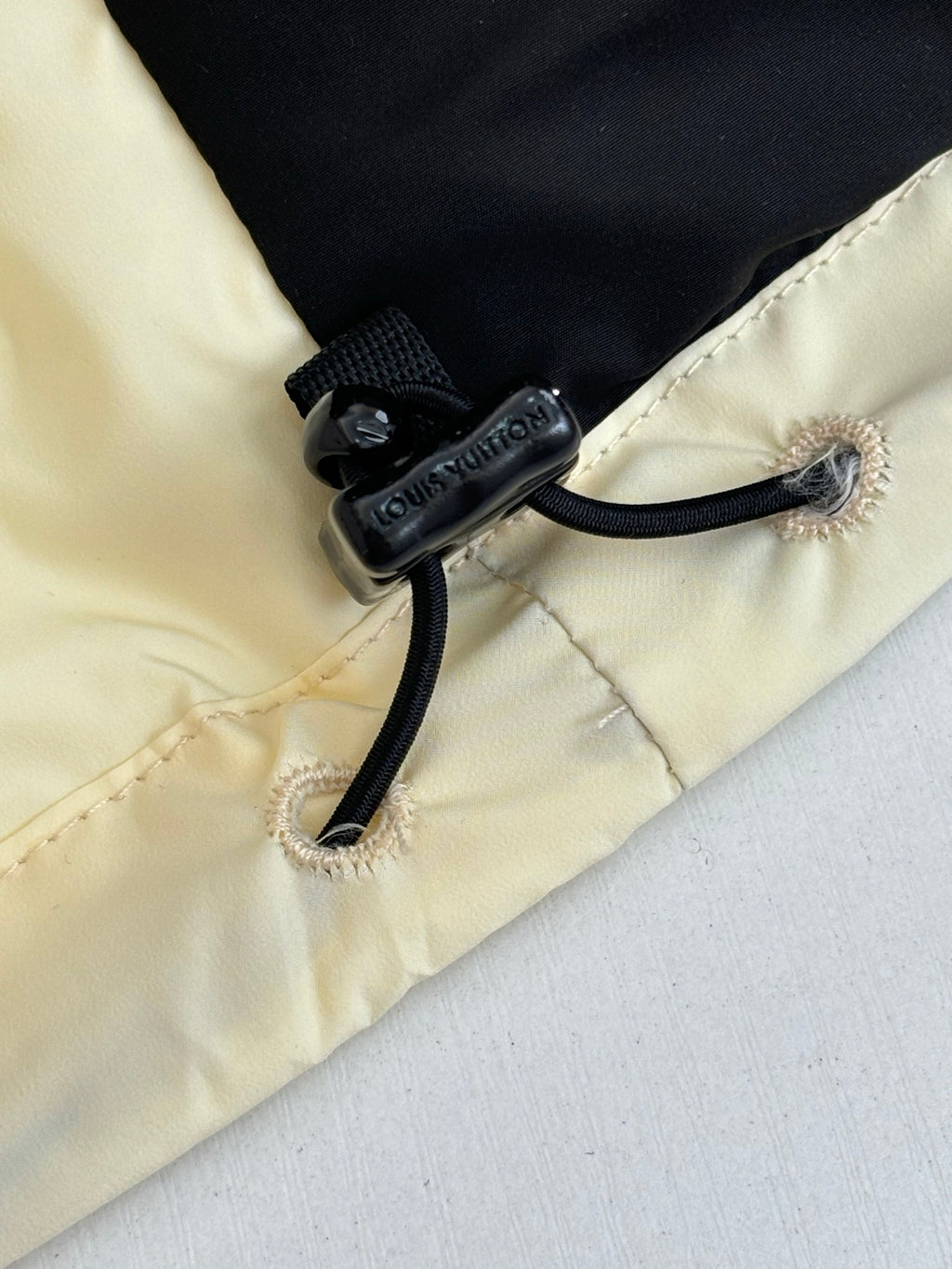 Cream puffer jacket cuff with black drawstring cord and embossed logo hardware
