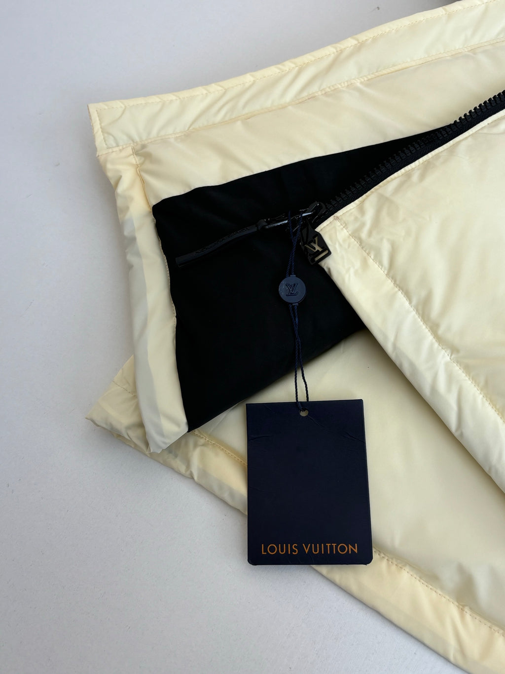 Cream puffer jacket pocket area with black inner panel and hanging Louis Vuitton tag