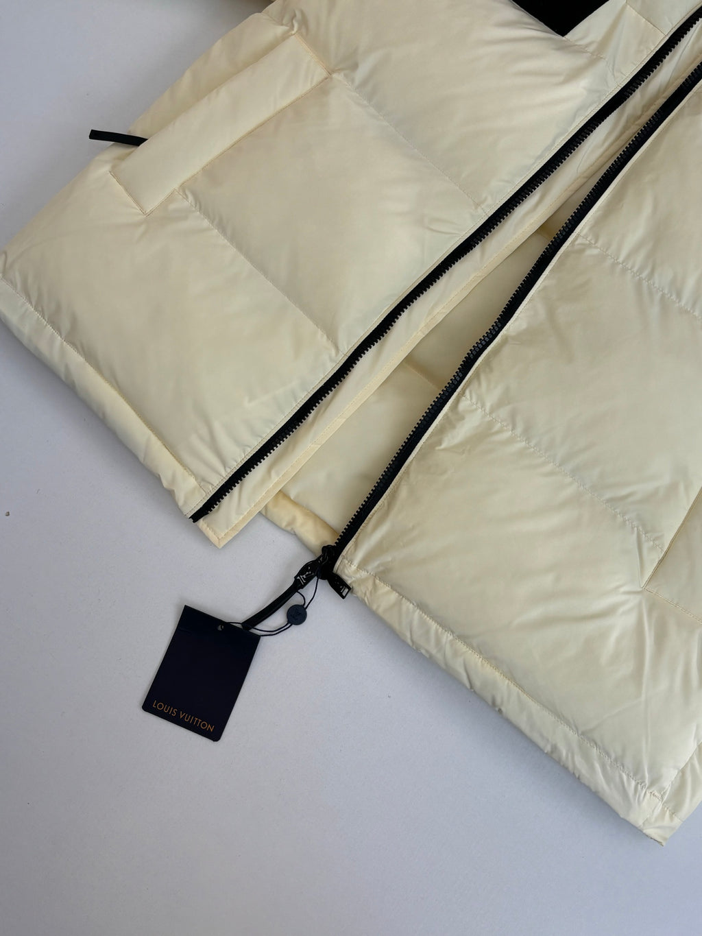 Cream puffer jacket detail with dual black zippers and hang tag