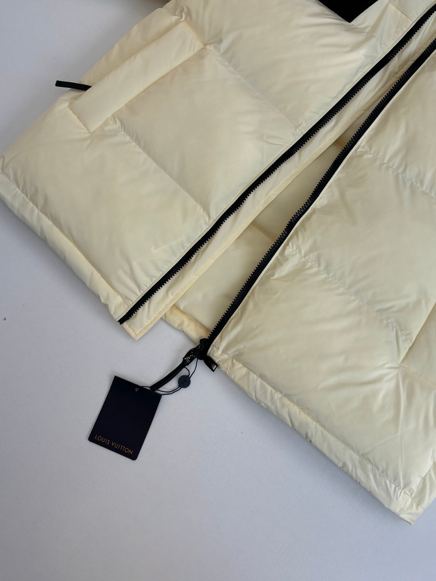 Cream puffer jacket detail with dual black zippers and hang tag