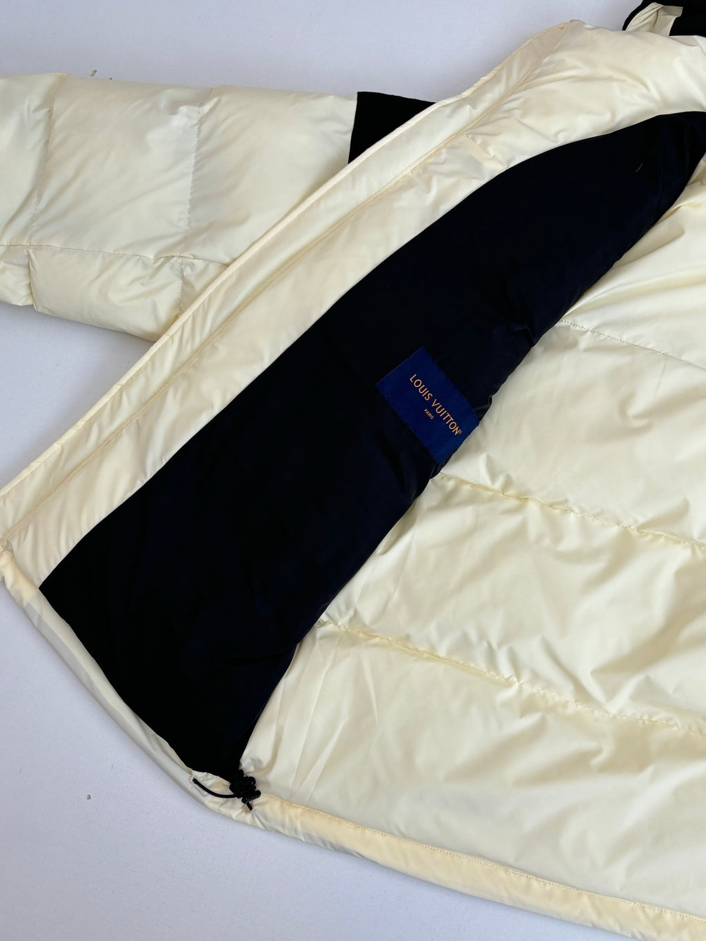 Two-tone puffer jacket laid flat, cream outer fabric with dark stripe panel