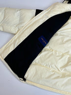 Two-tone puffer jacket laid flat, cream outer fabric with dark stripe panel