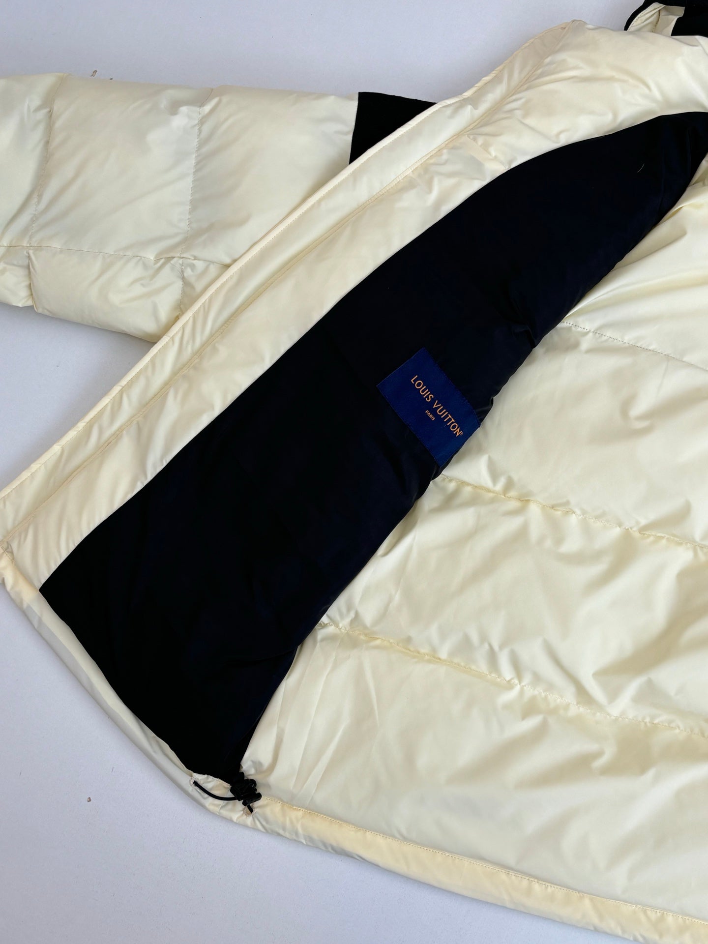Two-tone puffer jacket laid flat, cream outer fabric with dark stripe panel