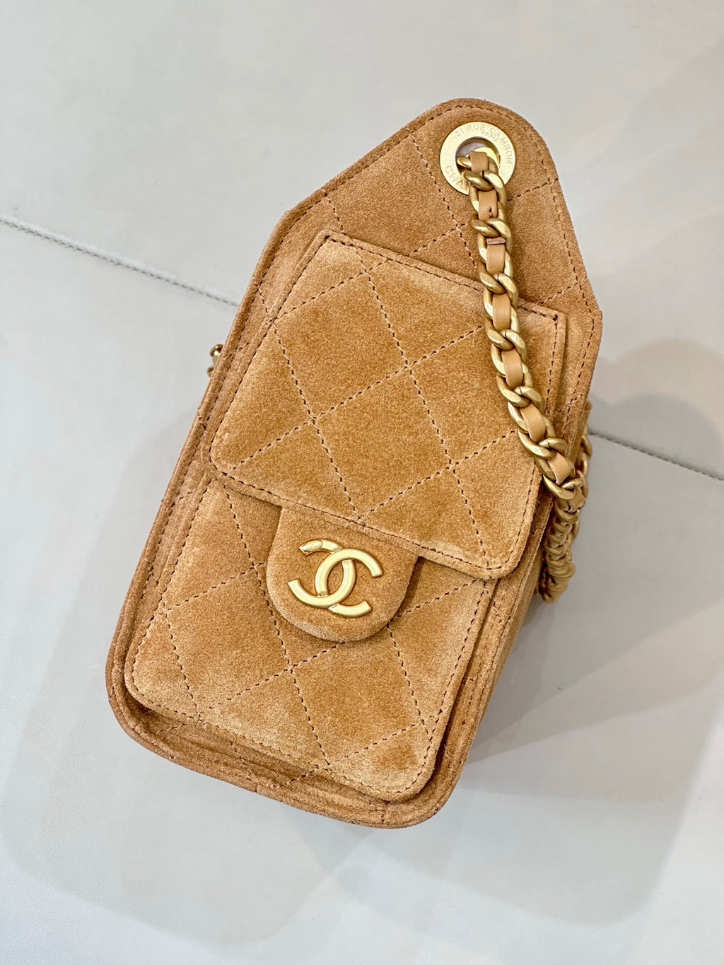 Tan suede small handbag with quilted design, gold logo plaque, and chain strap.