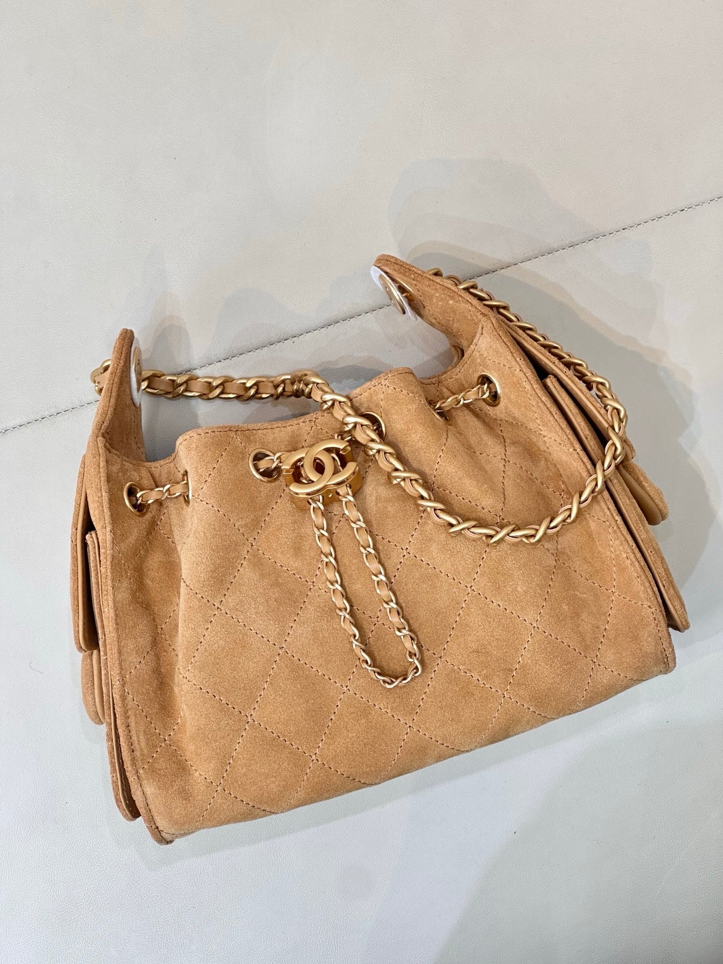 Tan quilted suede handbag with gold-tone chain strap and front logo charm detail.