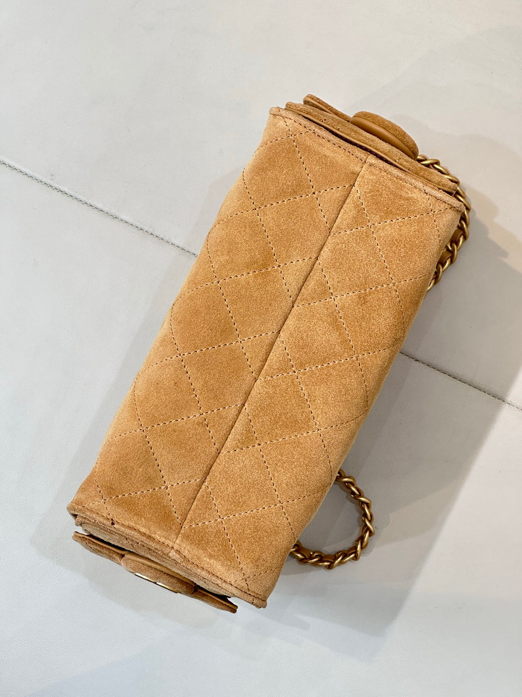 Tan quilted suede handbag with chain strap and folded side seam detail.