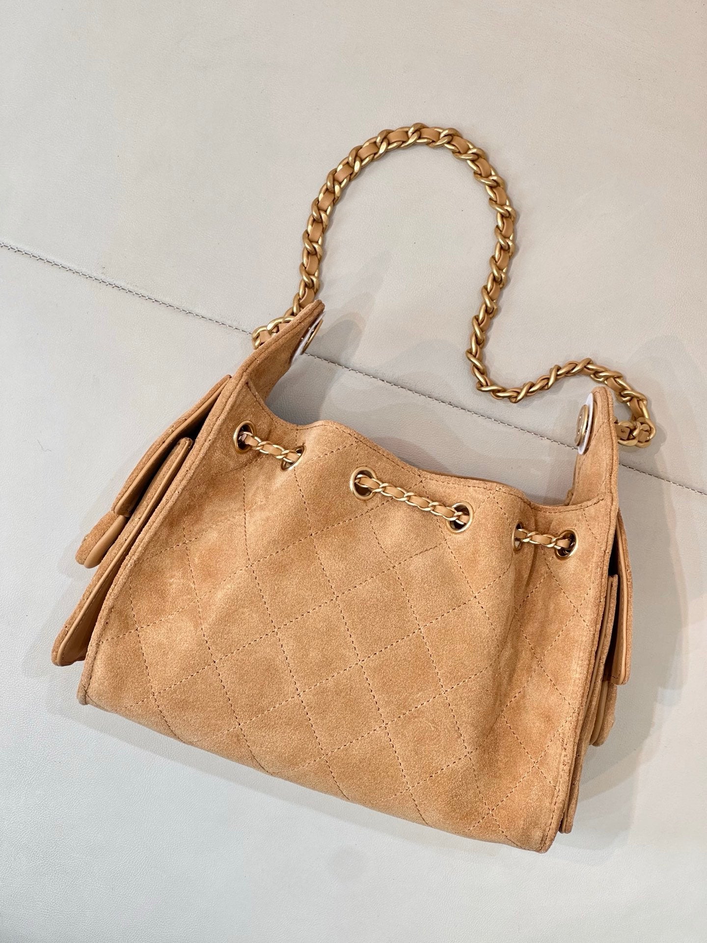 Tan quilted suede handbag with gold-tone chain strap and side flap with eyelets.