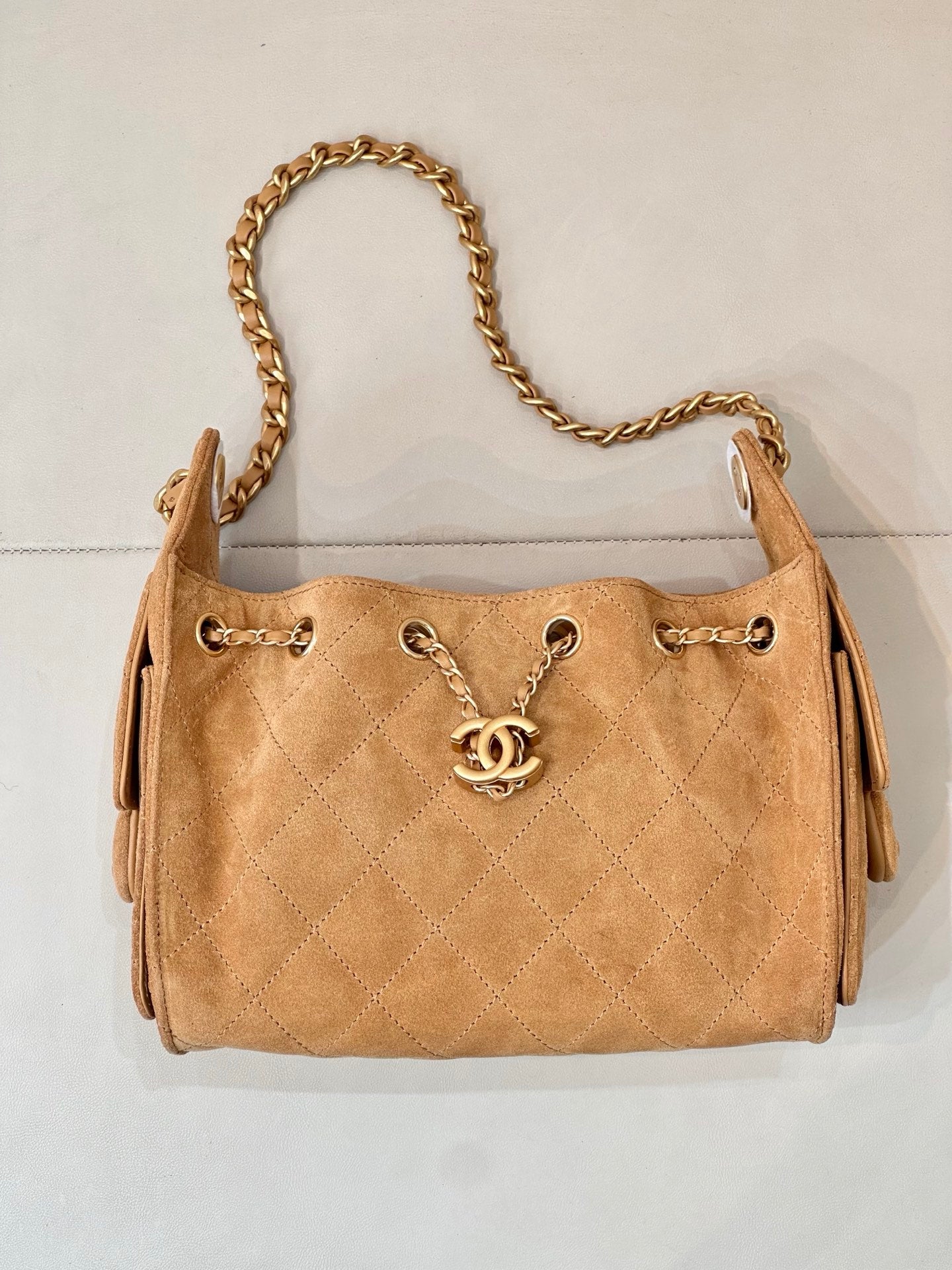 Tan quilted suede handbag with centered gold-tone logo and double strap chain.
