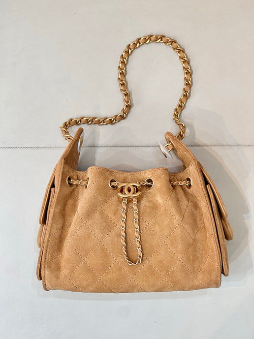 Tan quilted suede handbag with gold-tone chain handle and front logo emblem.