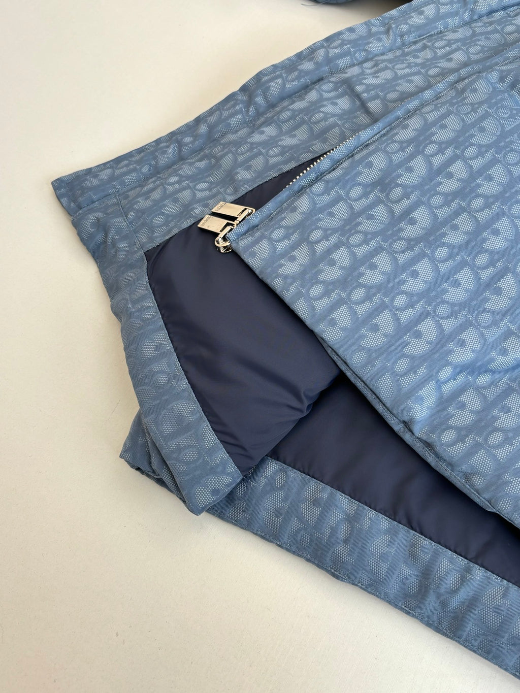 Blue Dior puffer jacket folded with gold zipper pulls and contrast inner panel