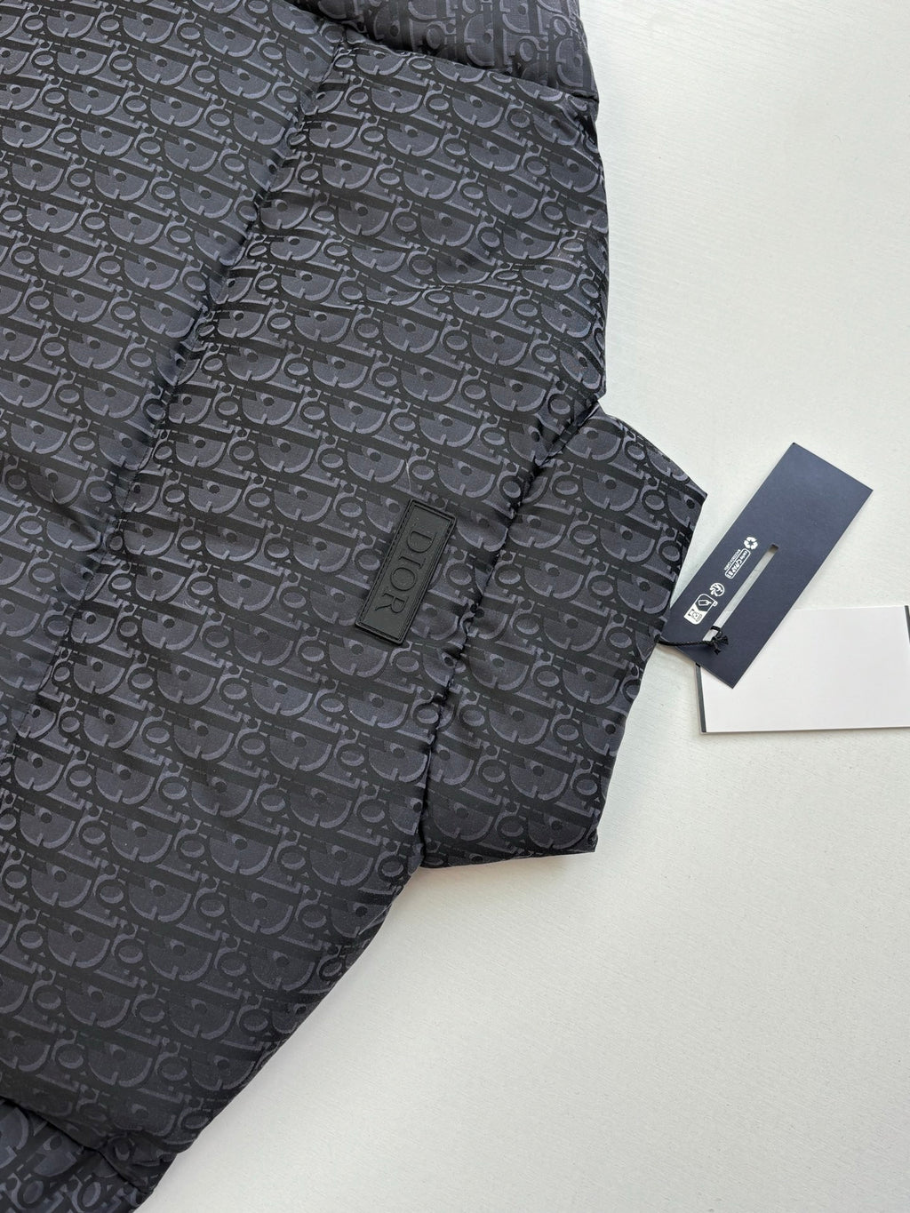Long quilted Dior jacket with standing collar, dark monogram pattern, tag attached.