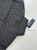 Long quilted Dior jacket with standing collar, dark monogram pattern, tag attached.