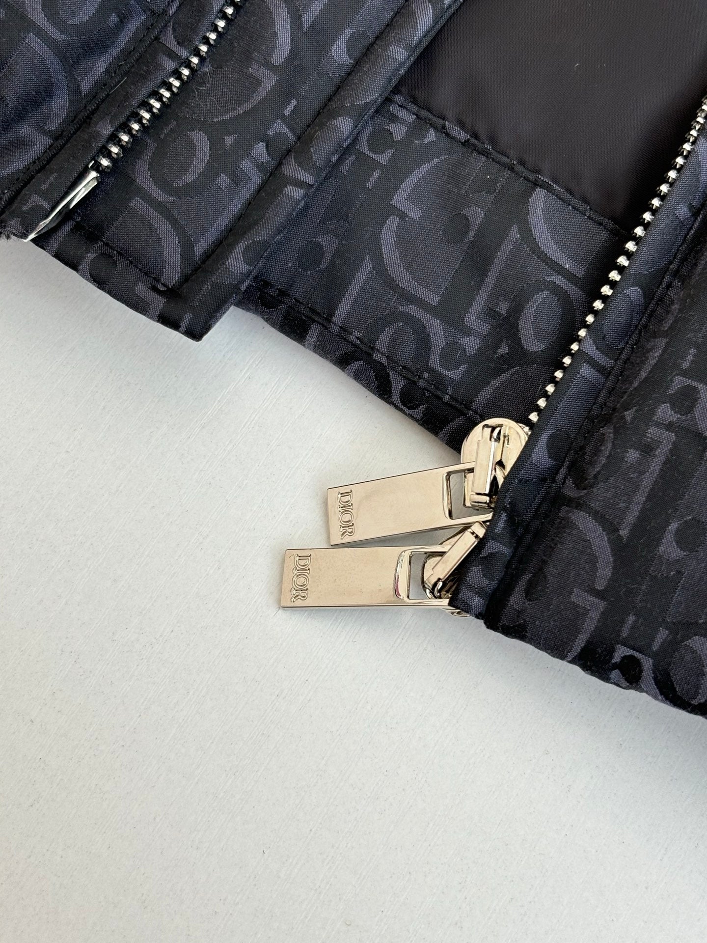 Dior jacket cuff with zipper and metal pull, dark monogram fabric close-up.