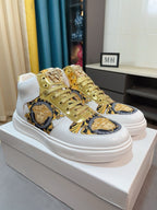 Pair of white mid-top sneakers with gold laces and blue-gold ornate Medusa panels