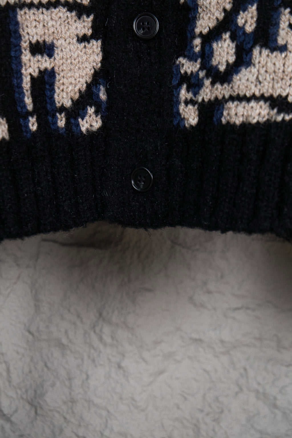 Dior knit cardigan close-up of black button placket and navy/cream logo pattern.