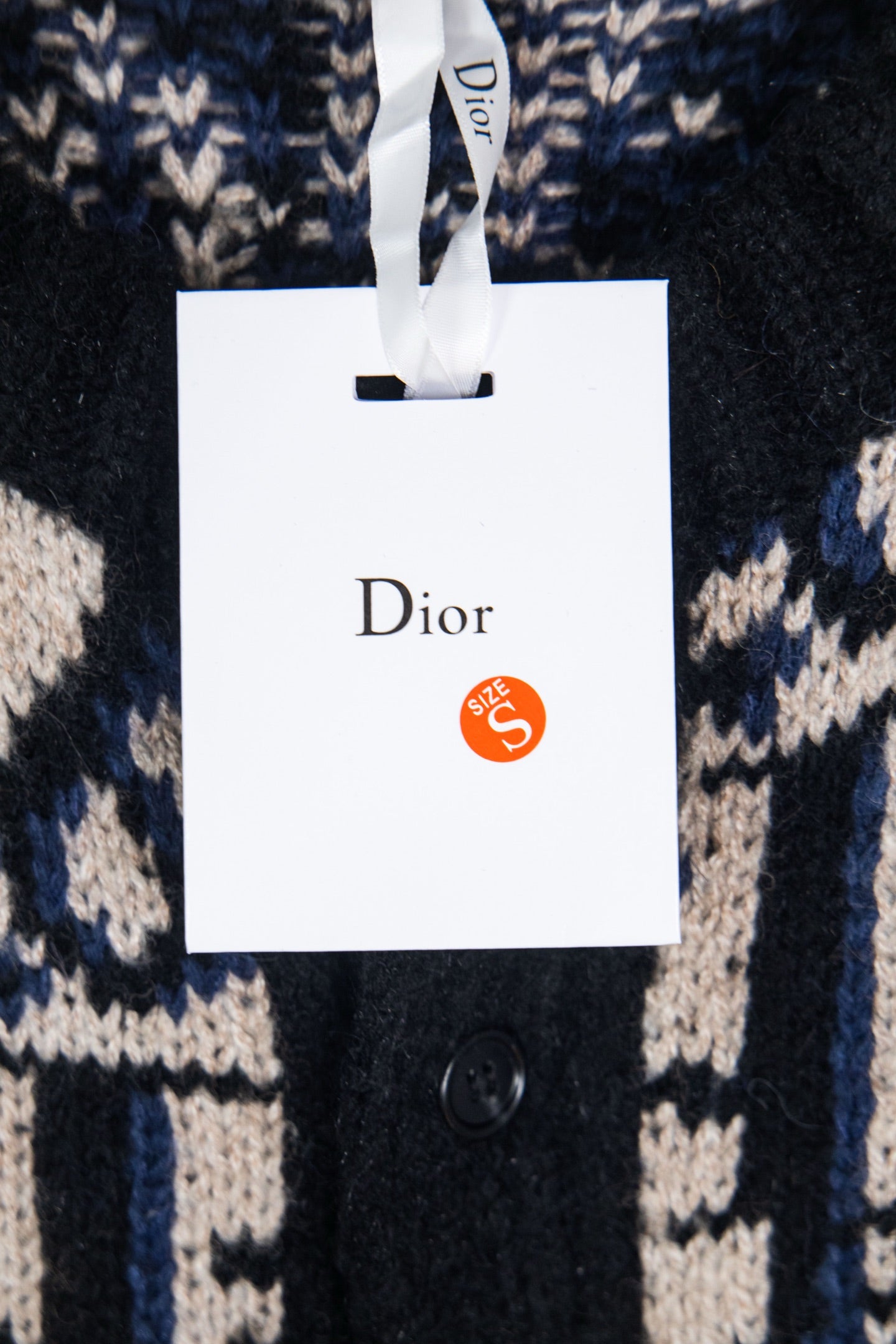 Dior knit cardigan with navy and cream geometric logo pattern, hanging tag visible.