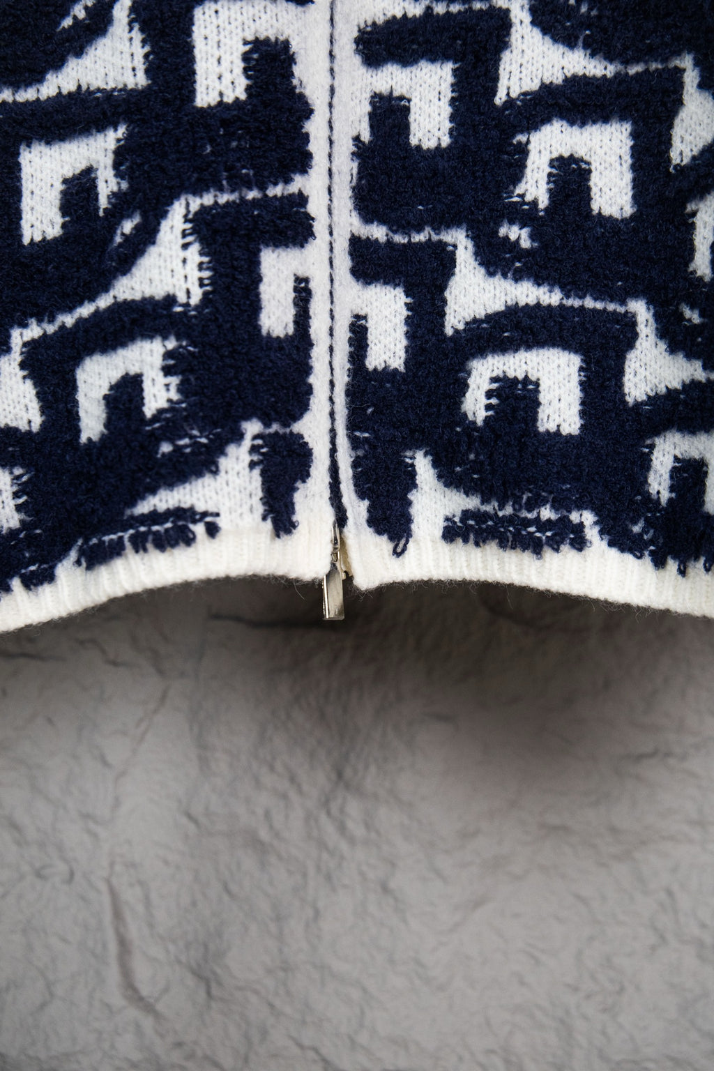 Bottom hem of navy-and-white knit sweater with ribbed trim and Dior motifs.