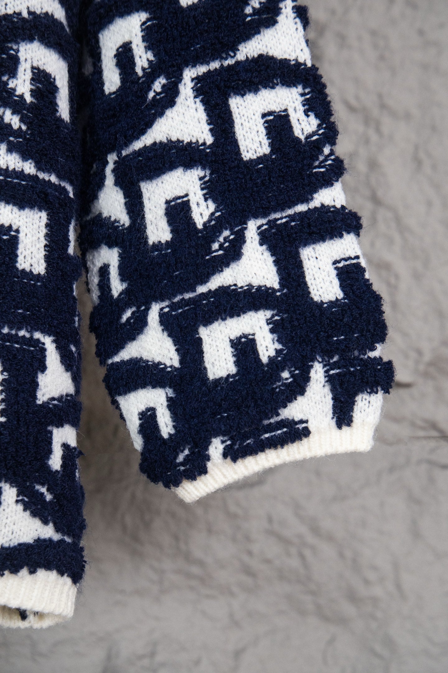 Lower sleeve and hem of navy-and-white patterned knit sweater with Dior motifs.