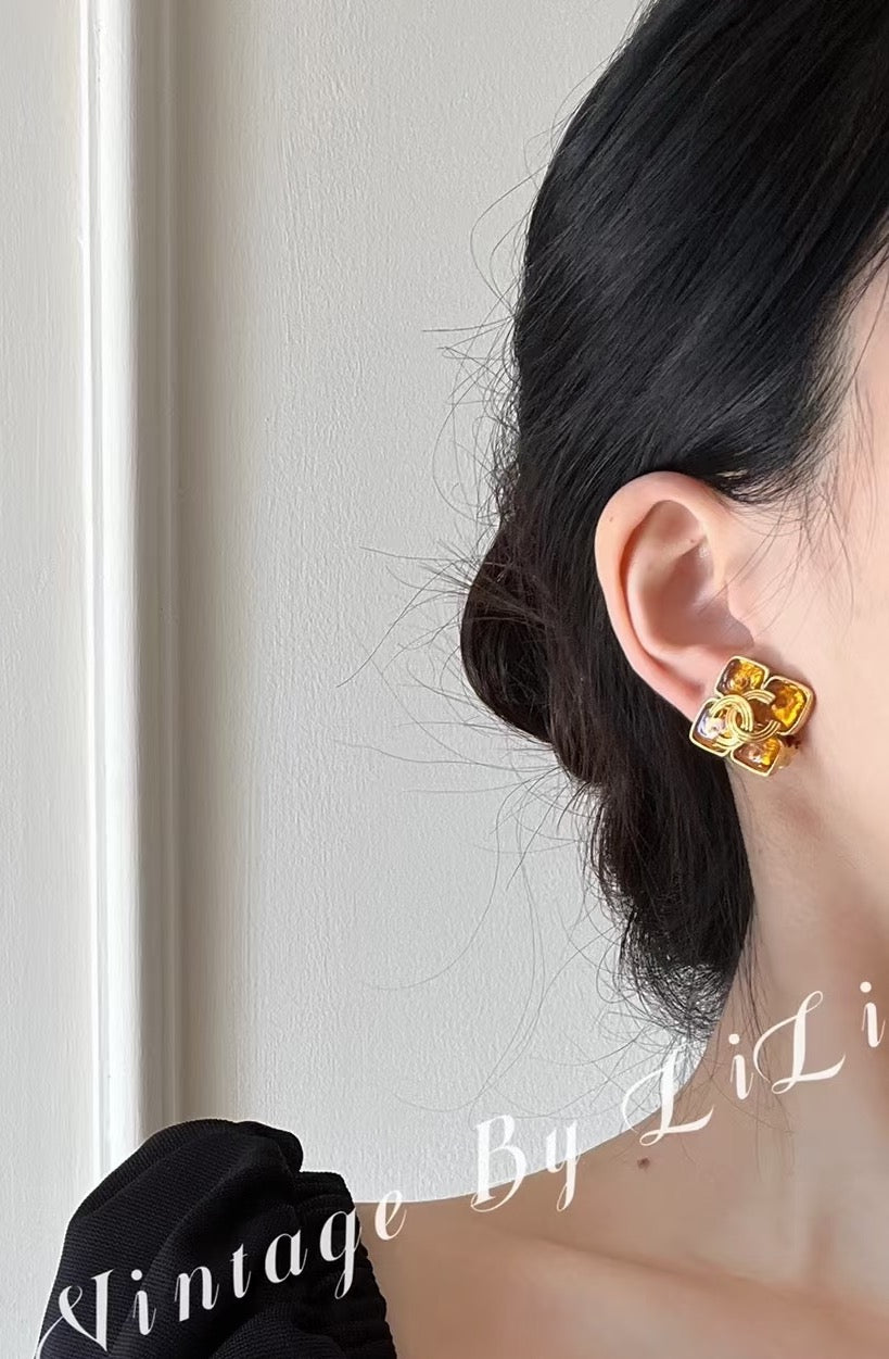 Gold-tone Chanel logo earrings on model ear, amber enamel studs visible