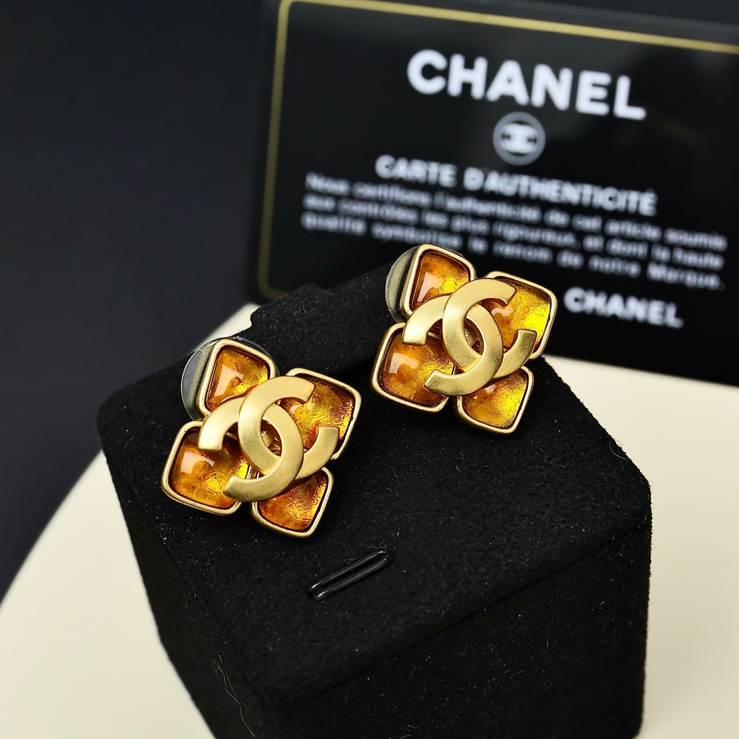 Gold-tone Chanel logo stud earrings with amber and black enamel, pair on cushion
