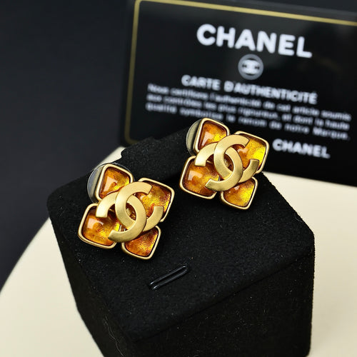 Gold-tone Chanel logo stud earrings with amber and black enamel, pair on cushion