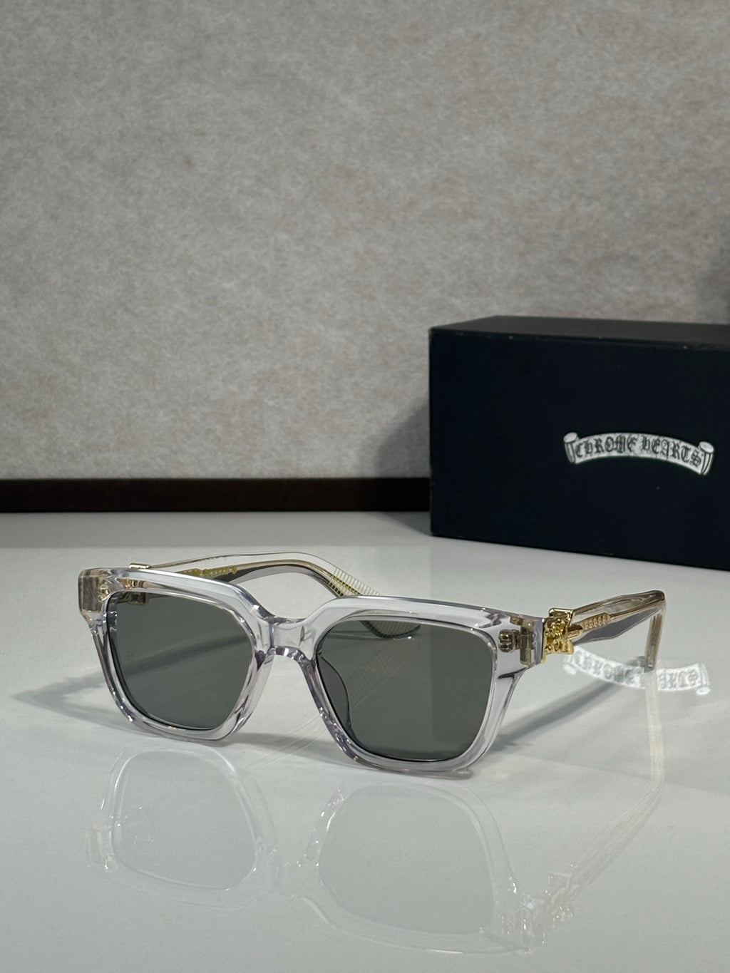Sunglasses with clear gray frames and dark green lenses, gold hinge detail on temples