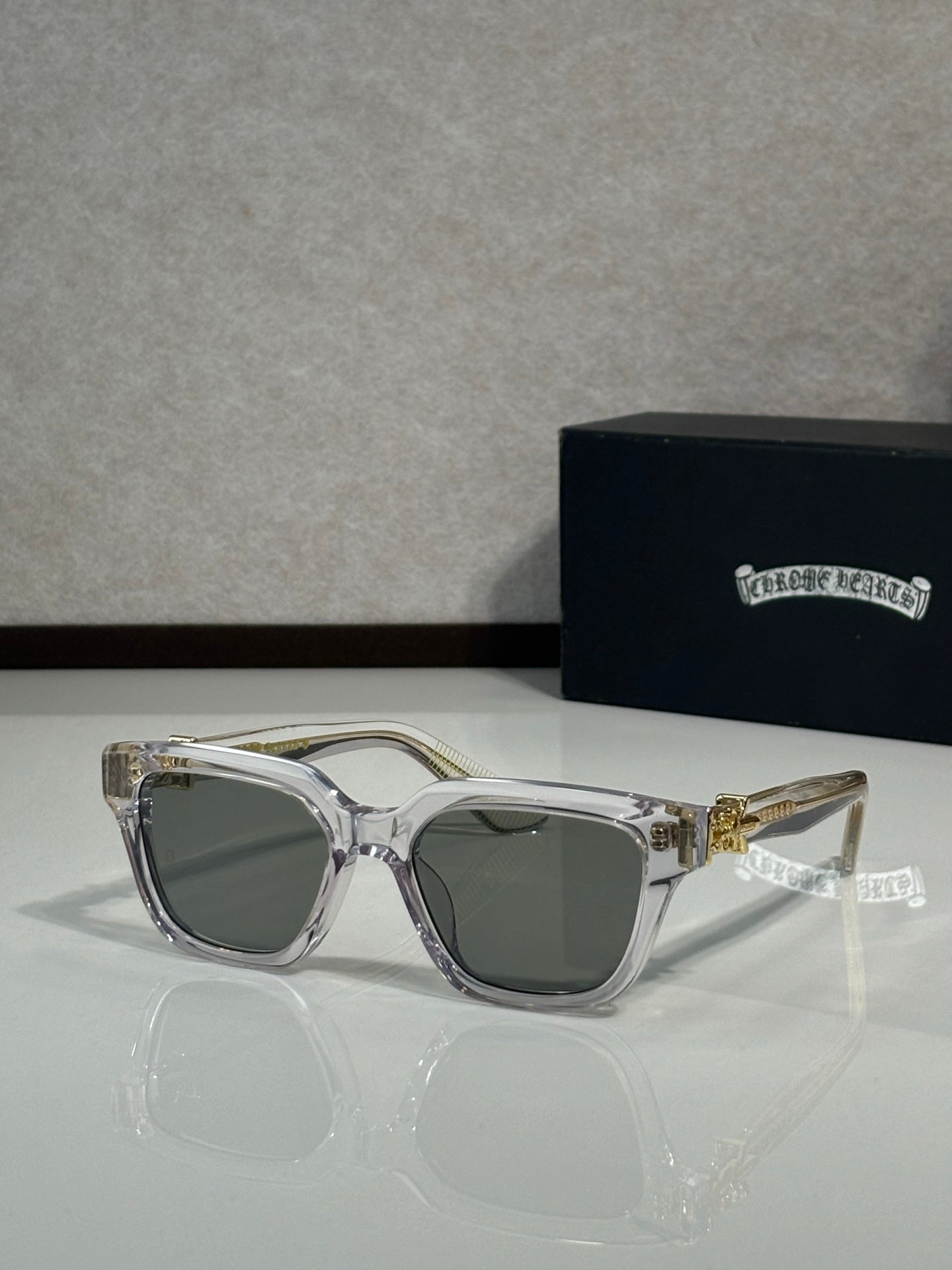 Sunglasses with clear gray frames and dark green lenses, gold hinge detail on temples