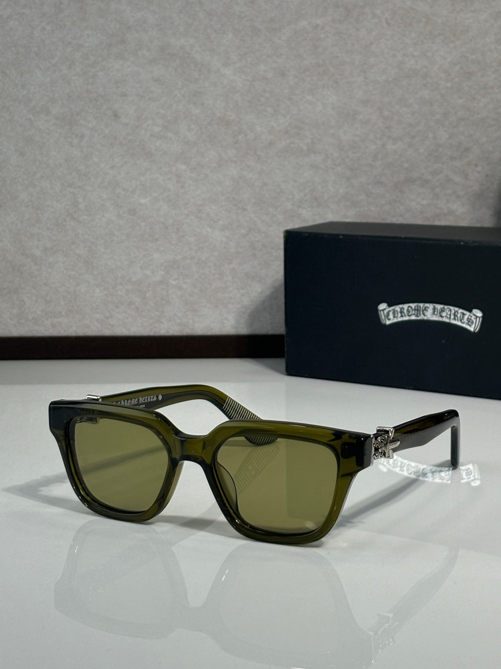 Sunglasses with olive frames and dark green lenses, metal hinge detail on temples