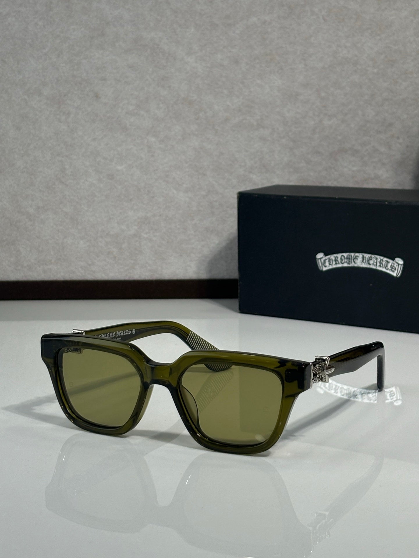 Sunglasses with olive frames and dark green lenses, metal hinge detail on temples