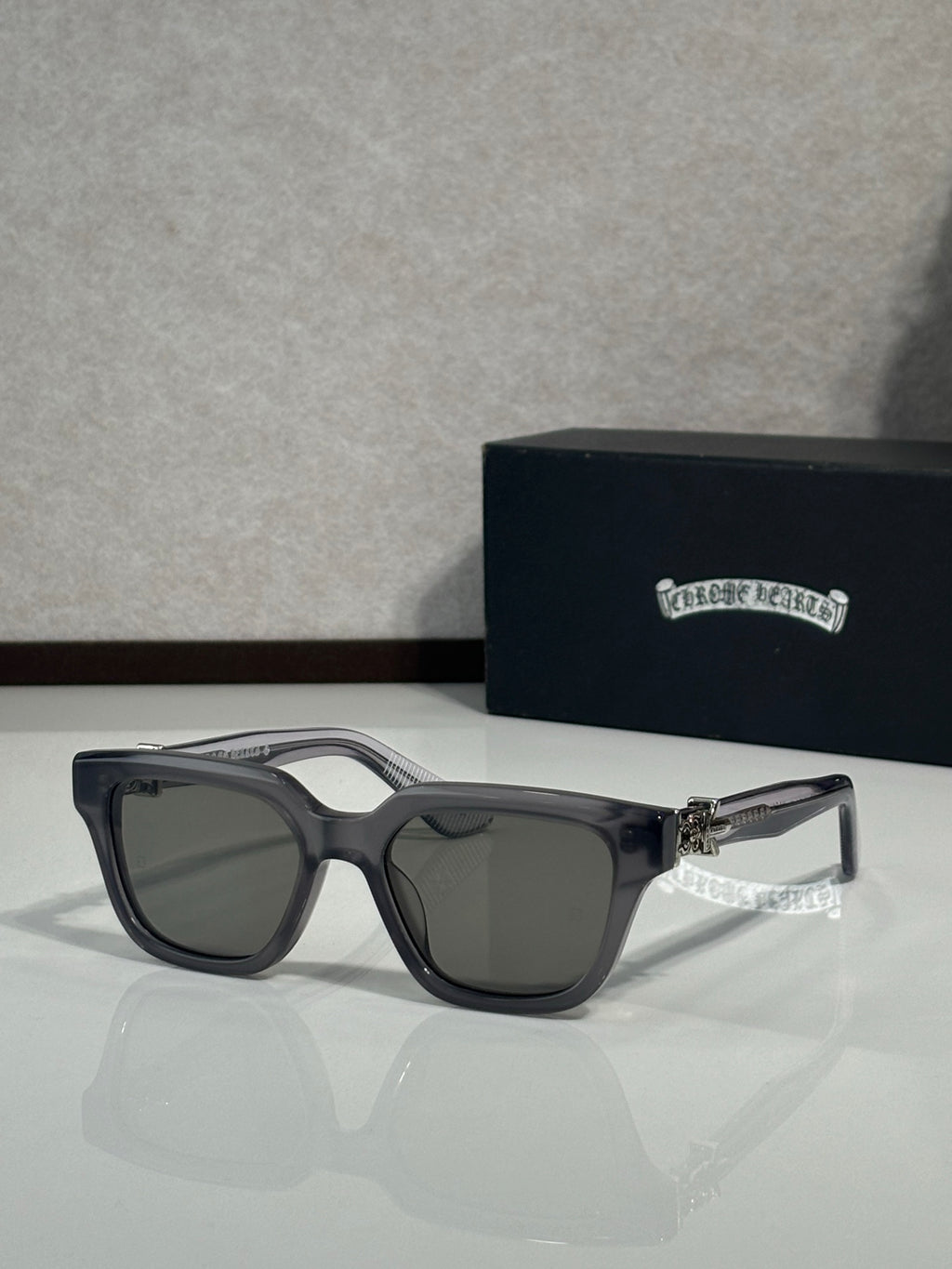 Sunglasses with clear gray frames and dark lenses, black temple accents and gold hinge