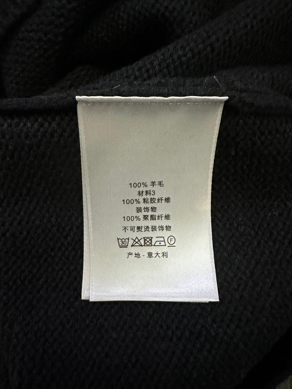 Clothing label inside black knit sweater with care text and fabric composition