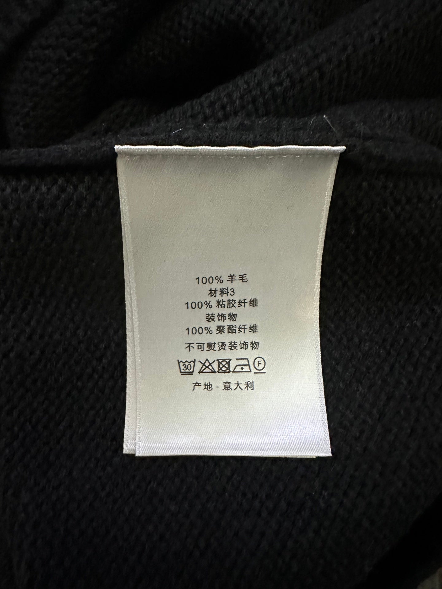Clothing label inside black knit sweater with care text and fabric composition