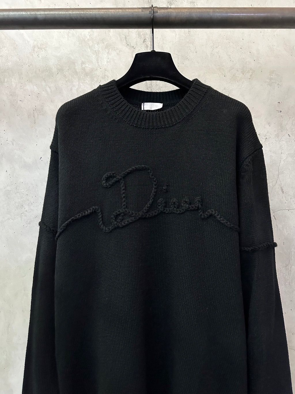 Black knit sweater with crew neck ribbing and prominent embroidered script logo on chest