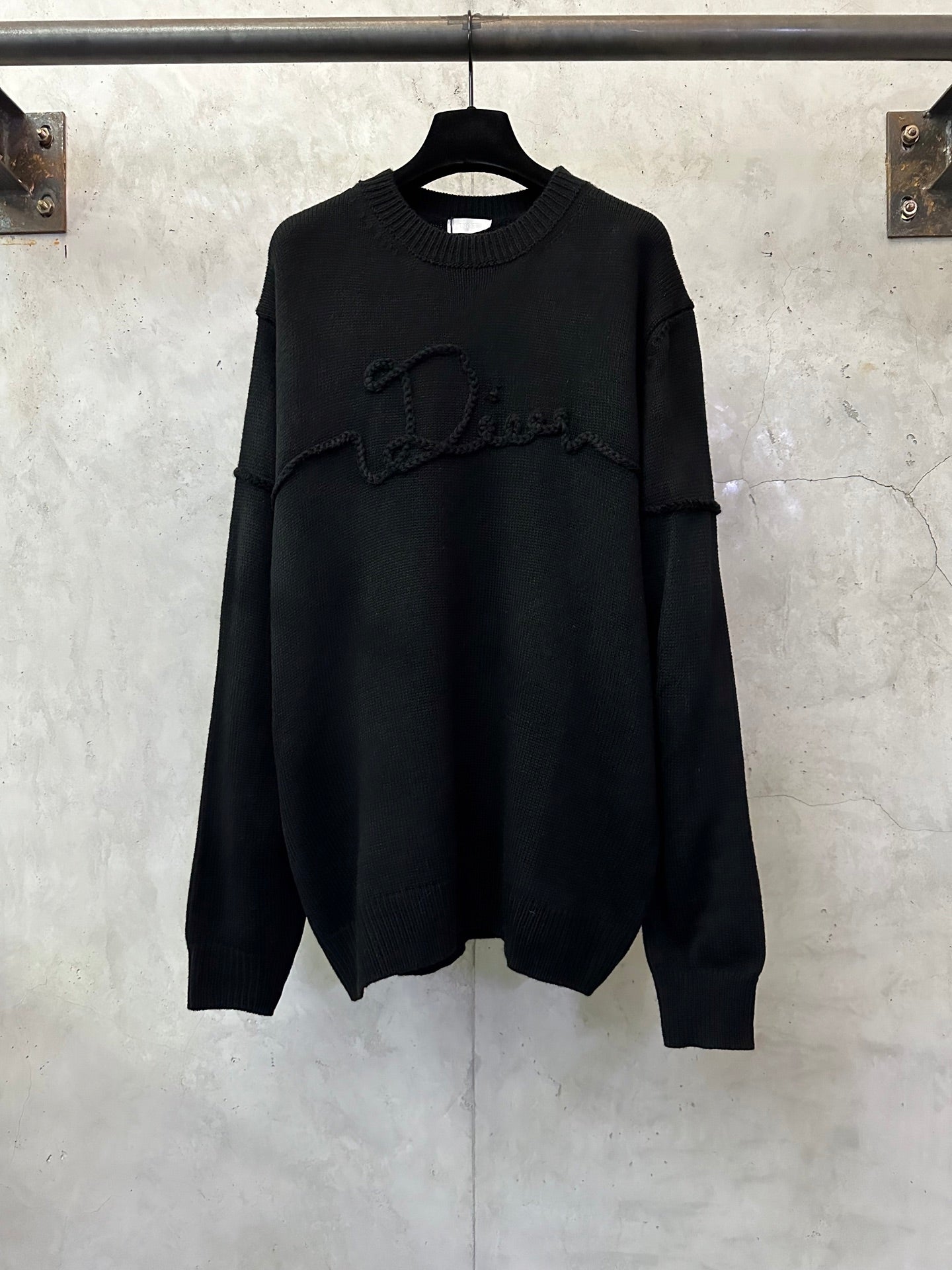 Black long-sleeve knit sweater with crew neck and embroidered logo across chest